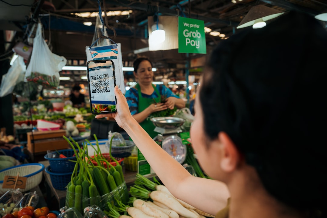 Eine Mitarbeiterin hält an einem Marktstand mit frischem Obst und Gemüse ein Smartphone in der Hand.